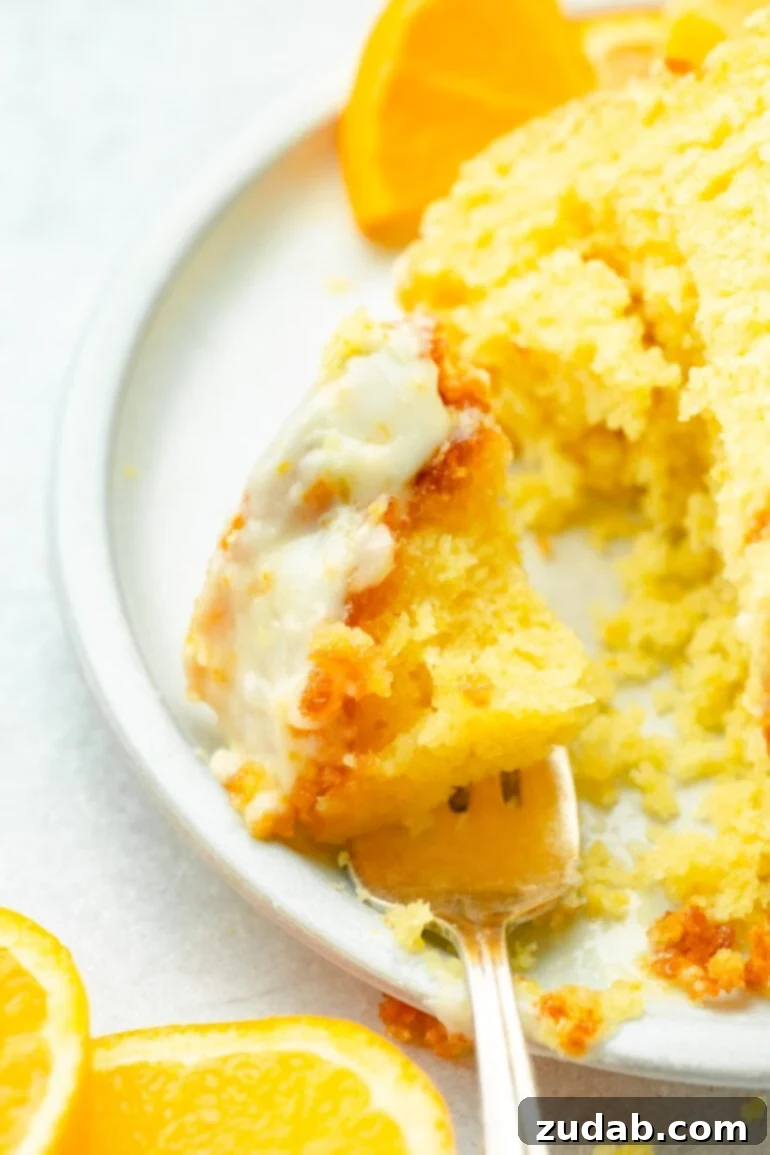 A close-up photo of a fork holding a bite of orange flavored pastry topped with a glossy white glaze, showcasing the pastry's delicate layers and vibrant citrus color.