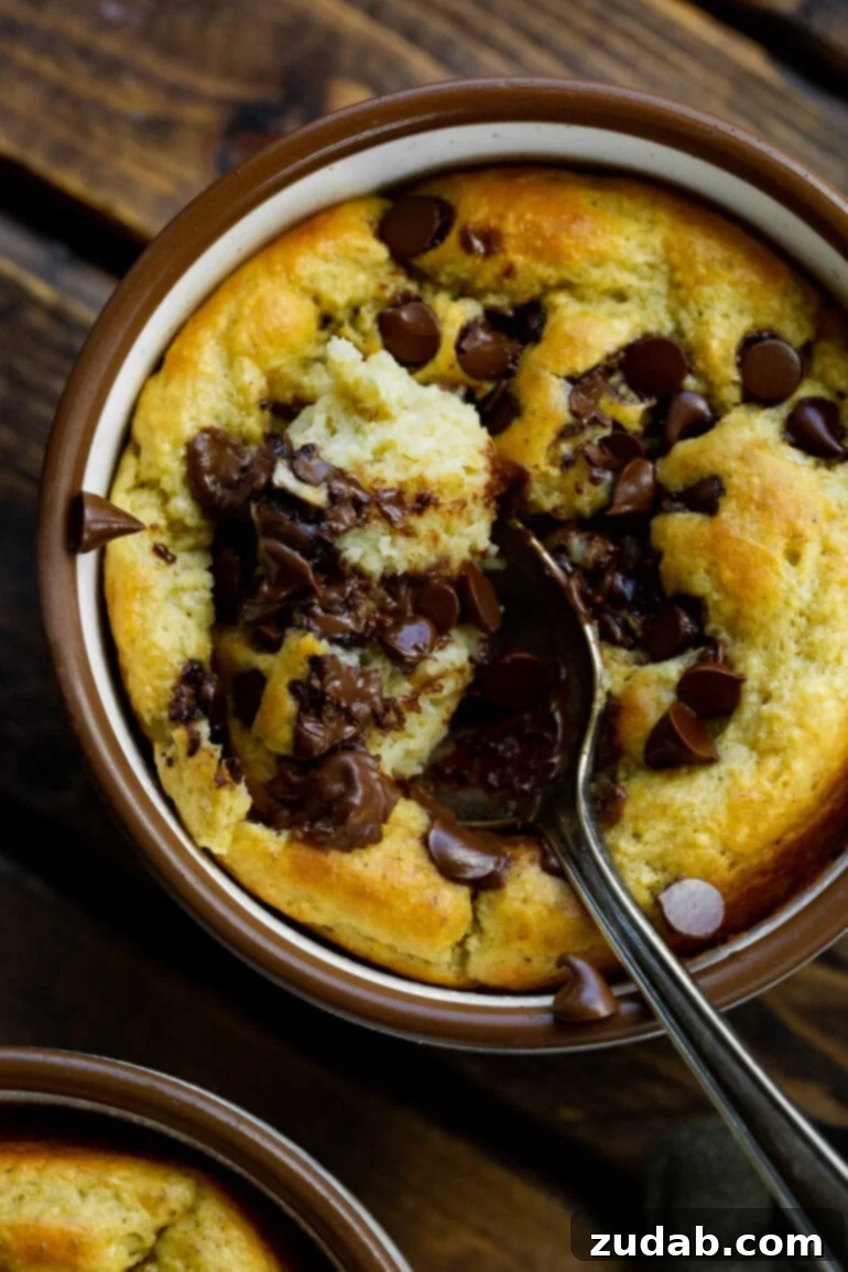 Choc Chip Cookie Protein Mug Bake 3 A spoon digging into a warm mug of baked chocolate chip oatmeal, revealing its soft, delicious interior.