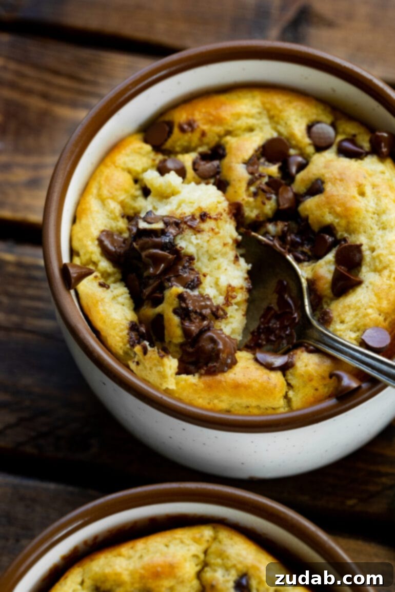 Choc Chip Cookie Protein Mug Bake 5 A spoon scooping a portion of golden baked oatmeal, garnished with mini chocolate chips, from a mug.