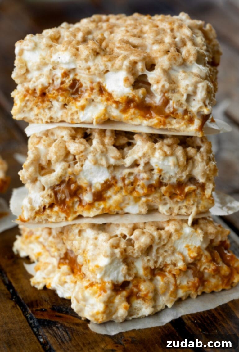 Nutty Brown Butter Caramel Krispie Delights 2 A photo of three dulce de leche stuffed gooey Rice Krispie Treats stacked on top of each other with little pieces of parchment paper between them, showcasing the delicious layers.