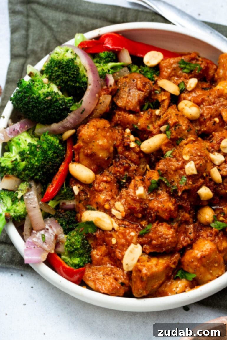 Irresistible Peanut Butter Chicken 2 a photo of saucy peanut butter chicken topped with chopped peanuts and a side of broccoli, red onion slices and red pepper slices