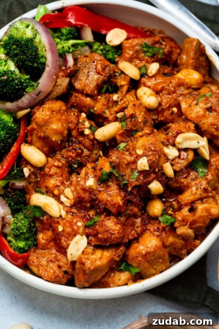 Irresistible Peanut Butter Chicken 3 a photo of a large white bowl full of saucy peanut butter chicken topped with chopped peanuts and cilantro.