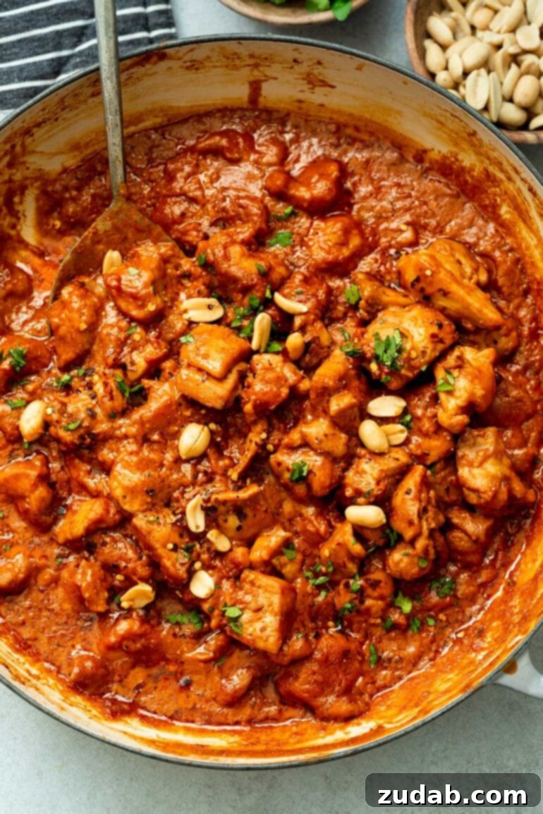 Irresistible Peanut Butter Chicken 7 a photo of a large skillet full of chicken chunks being simmered in a thick peanut butter sauce topped with fresh cilantro and chopped peanuts