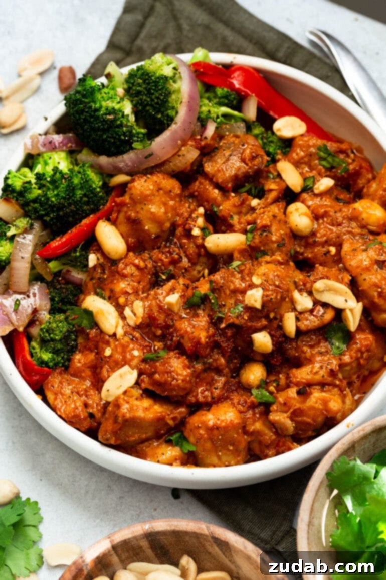 Irresistible Peanut Butter Chicken 8 a photo of a large bowl full of peanut butter chicken with a broccoli salad on the side and topped with peanuts and cilantro.