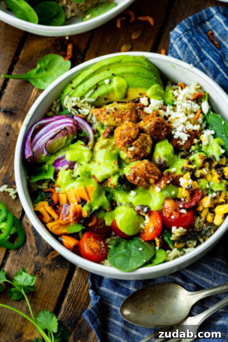 Fiesta Chicken Bowl 3 A vibrant Mexican chicken burrito bowl brimming with colorful ingredients: bright orange and red bell peppers, crisp red onion, creamy avocado slices, generous chunks of perfectly seasoned chicken, all generously topped with a luscious, fresh green avocado creamy dressing.