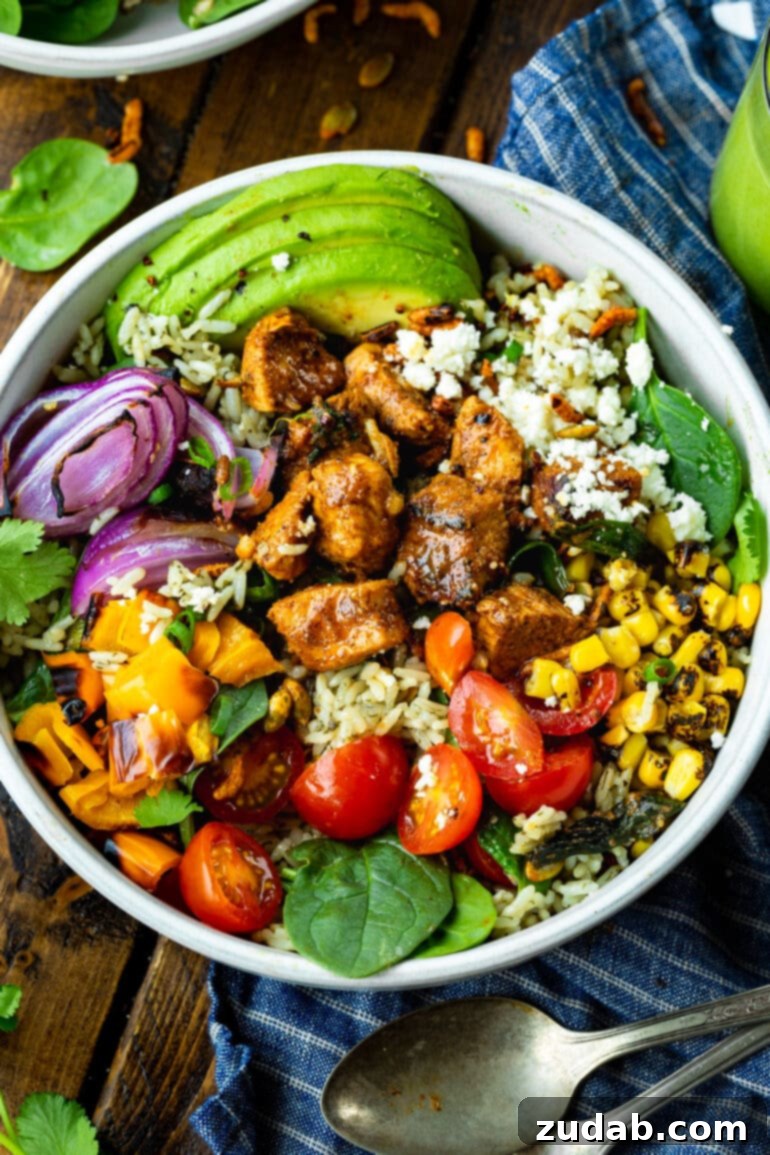 Fiesta Chicken Bowl 6 A beautifully presented chicken burrito bowl, generously topped with savory seasoned chicken chunks, perfectly roasted corn, vibrant cherry tomatoes, creamy avocado slices, crisp red onions, and a sprinkle of crumbled queso fresco for a finishing touch.