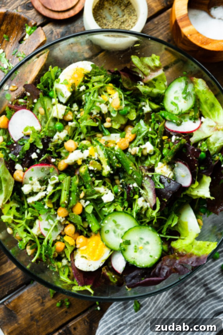 Effortless Springtime Greens 6 a photo of a spring salad consisting of cucumbers, radishes, asparagus, greens, hard boiled eggs, roasted chickpeas, and toasted pine nuts.