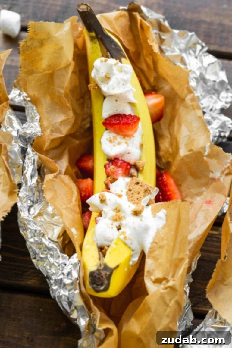 Ultimate Campfire Banana Boats 5 A gourmet Strawberry Shortcake banana boat, beautifully presented in parchment paper and foil, featuring roasted banana, fresh strawberries, crushed Nilla Wafers, and a dollop of whipped cream.