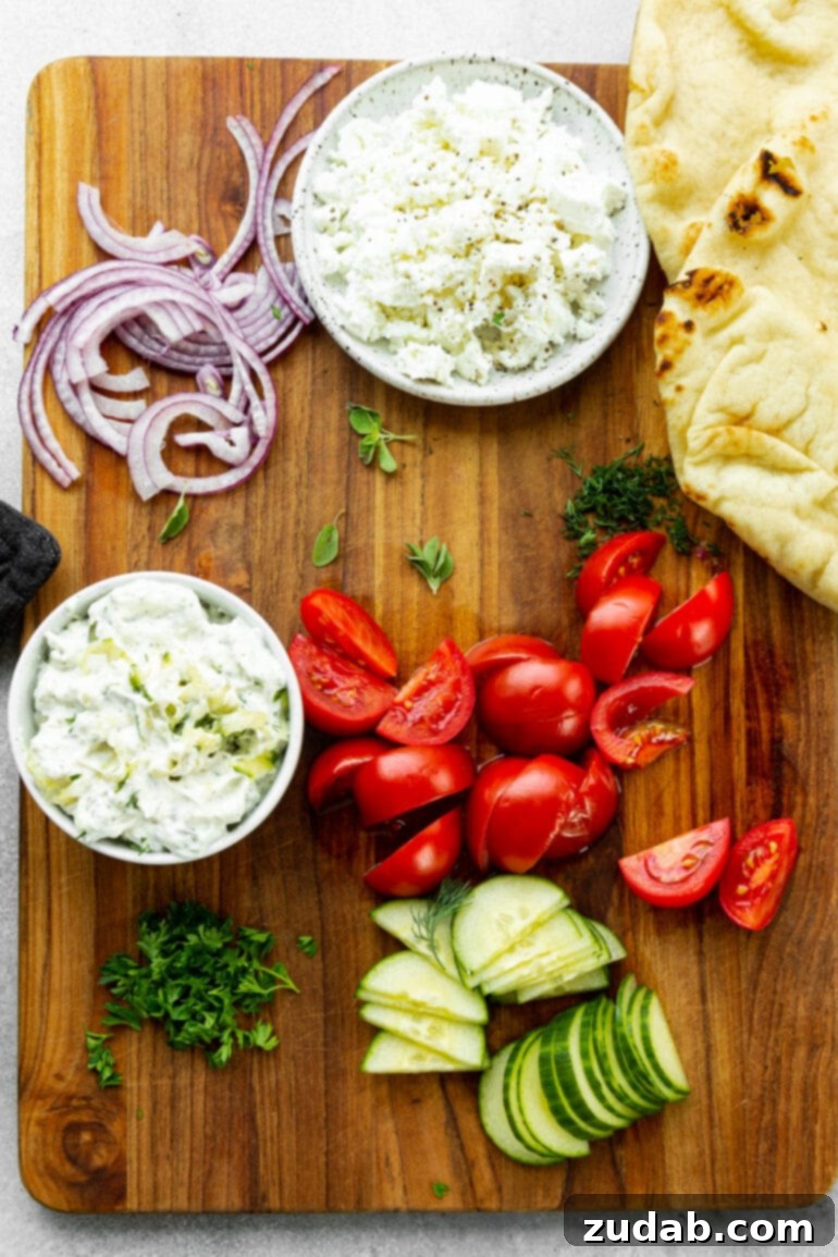 Cades Signature Chicken Gyros 4 A bountiful spread of fresh and colorful gyro toppings, meticulously arranged on a platter. Sliced tomatoes, crisp cucumber, vibrant fresh parsley, thinly sliced red onions, a generous pile of crumbled feta cheese, and a creamy bowl of tzatziki sauce await assembly.