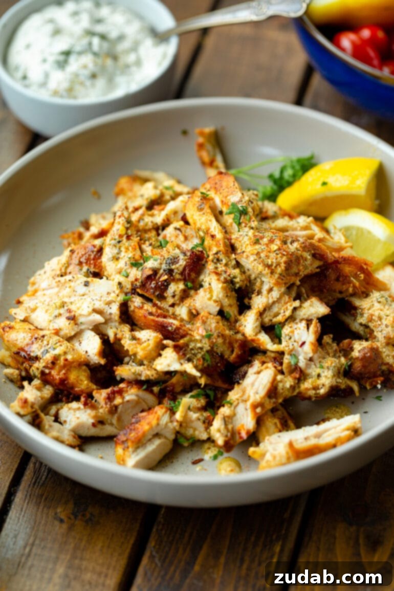 Cades Signature Chicken Gyros 8 A close-up photo of freshly sliced, baked, and seasoned chicken thighs arranged artfully on a plate, garnished with vibrant fresh parsley and bright lemon wedges. The chicken is tender and ready to be served.