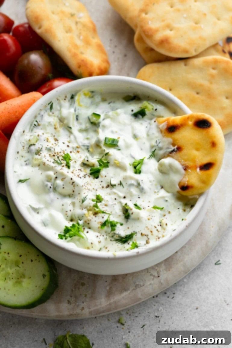 The Perfect Homemade Tzatziki 2 A small bowl of creamy tzatziki sauce with a piece of pita bread dipped into it, highlighting its rich texture and perfect consistency, ready for dipping and spreading.