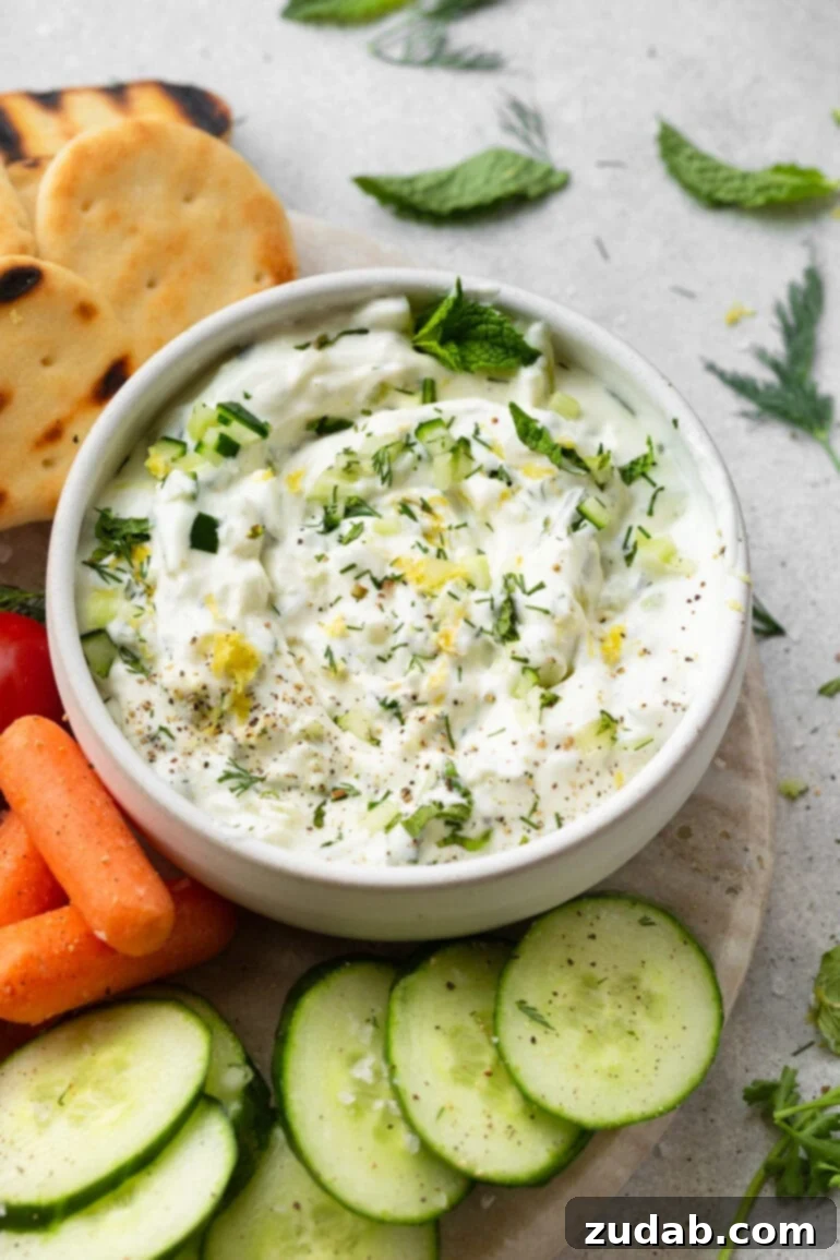 The Perfect Homemade Tzatziki 4 A small bowl of fresh homemade tzatziki sauce surrounded by a colorful array of fresh vegetables and pieces of warm pita bread, perfect for dipping.