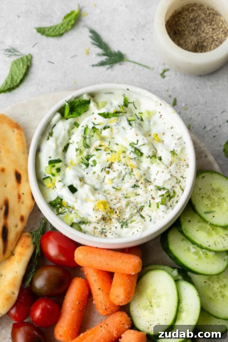 The Perfect Homemade Tzatziki 5 A small ceramic bowl of creamy tzatziki sauce surrounded by an abundance of colorful fresh vegetables and small pieces of warm naan bread, ready for sharing.