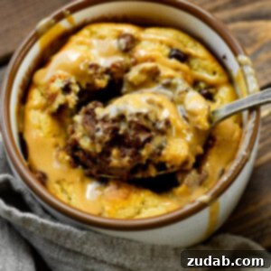 a photo of a mug full of baked oatmeal peanut butter and chocolate mug cake and someone is removing a spoonful of cake from the middle.