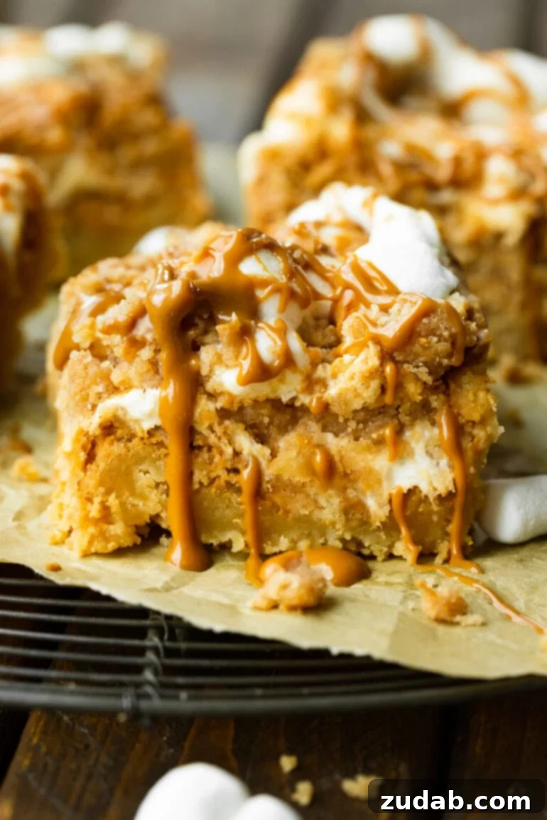 Ultimate Gooey Biscoff Crumb Bars 2 A photo of a Biscoff crumb bar sitting on a torn piece of parchment paper, showcasing its rich layers: a thick cookie base, melted marshmallows, and crumb topping drizzled with cookie butter.