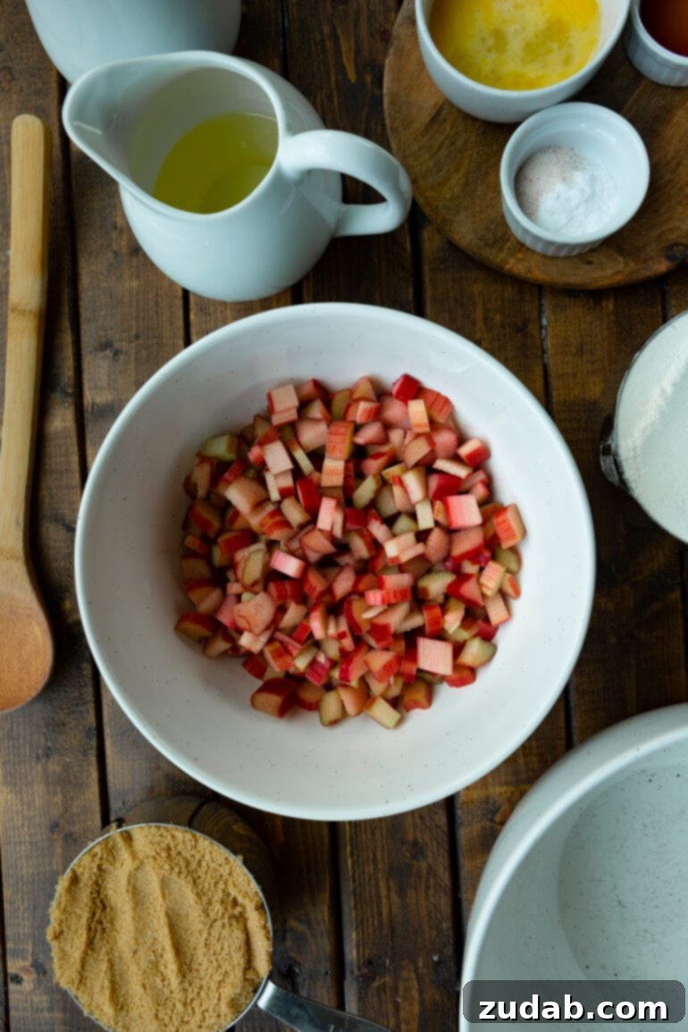 Sweet and Tart Rhubarb Cake 5 A photo of a bowl full of chopped rhubarb surrounded by the other ingredients for making rhubarb cake.