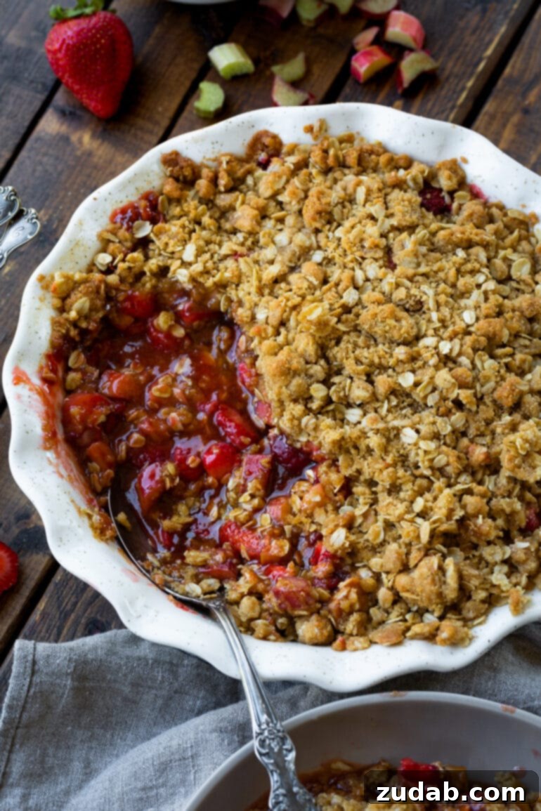 Golden Strawberry Rhubarb Crisp 7 A delicious photo of a strawberry rhubarb crisp in a round baking dish, with a serving scooped out, revealing the vibrant red, juicy filling and the crunchy, buttery oat topping underneath.