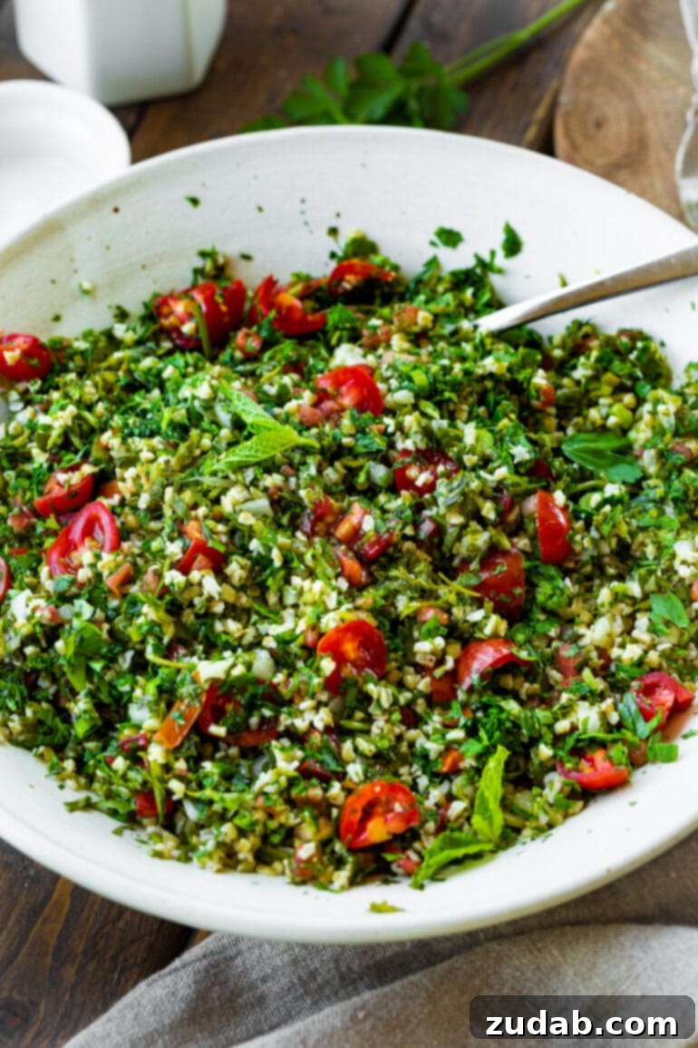 Bright and Flavorful Tabbouleh 6 A large, elegant white serving bowl filled to the brim with freshly prepared tabbouleh salad, with a silver serving spoon invitingly placed within it.