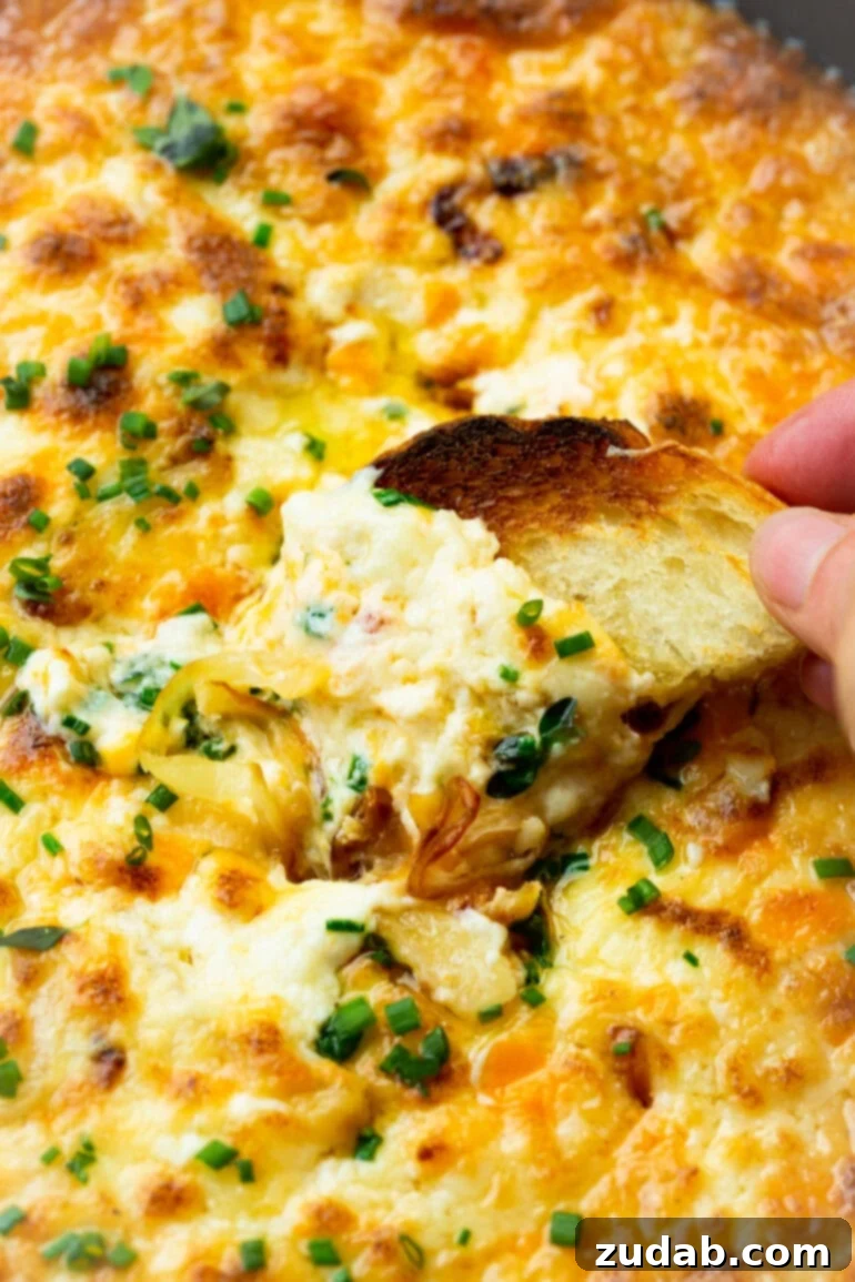 Golden Gooey Onion Cheese Dip 3 A photo of someone scooping creamy cheesy onion dip with a toasted piece of bread, showcasing the rich texture.