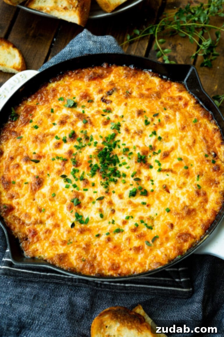 Golden Gooey Onion Cheese Dip 4 A large cast iron skillet brimming with baked cheesy onion dip, garnished with minced fresh herbs, ready for serving.