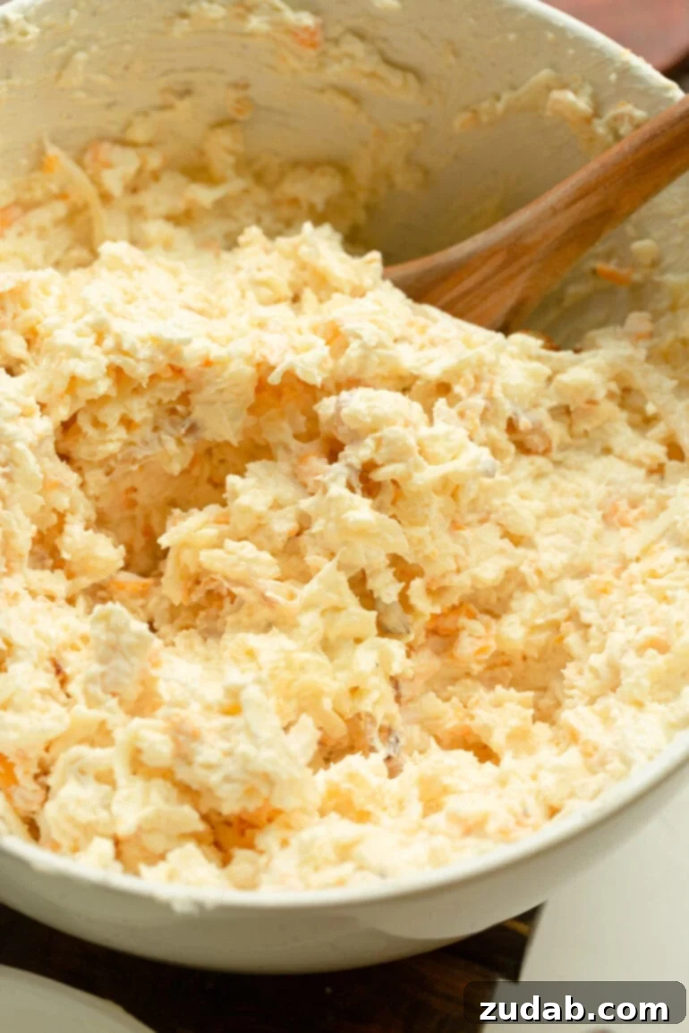 Golden Gooey Onion Cheese Dip 5 A wooden spoon stirring a creamy mix of five cheeses and caramelized onions in a mixing bowl for baked onion cheese dip.