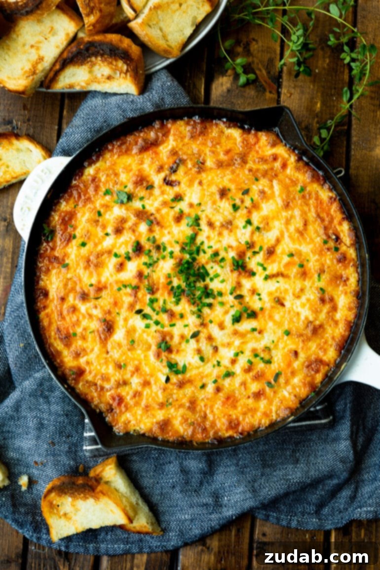 Golden Gooey Onion Cheese Dip 7 An overhead shot of a cast iron skillet filled with golden baked cheesy onion dip, topped with finely minced chives.