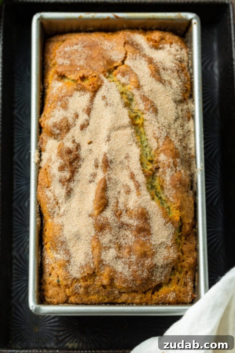 Ultimate Banana Zucchini Bread 3 A photo of a whole loaf of golden brown baked banana zucchini bread, still in its pan, with a delicate cinnamon sugar topping.