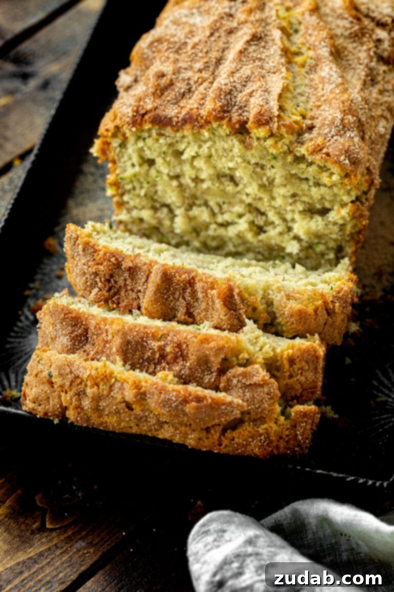 Ultimate Banana Zucchini Bread 4 A photo of a freshly baked loaf of golden banana zucchini bread with the first few slices expertly cut and tipped onto each other, revealing its moist interior.