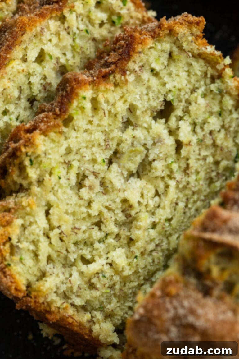 Ultimate Banana Zucchini Bread 6 A close-up photo of a single slice of banana zucchini bread, perfectly golden and topped with cinnamon sugar, revealing its tender, moist interior.