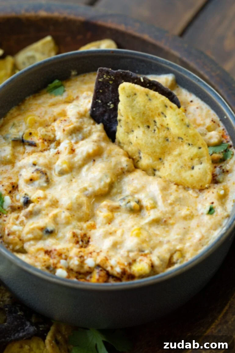 Creamy Slow Cooker Elote Dip 5 a photo of two tortilla chip dipped into a bowl of cream mexican street corn dip.