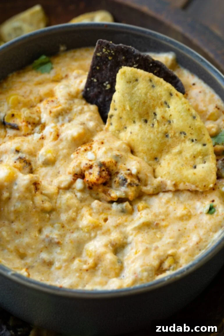 Creamy Slow Cooker Elote Dip 8 a photo of a bowl of creamy mexican street corn dip with two tortilla chips dipped into it.