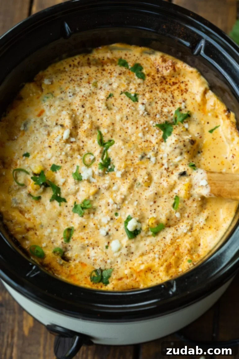 Creamy Slow Cooker Elote Dip 10 a photo of a wooden spoon stirring a crock pot full of mexican street corn dip.