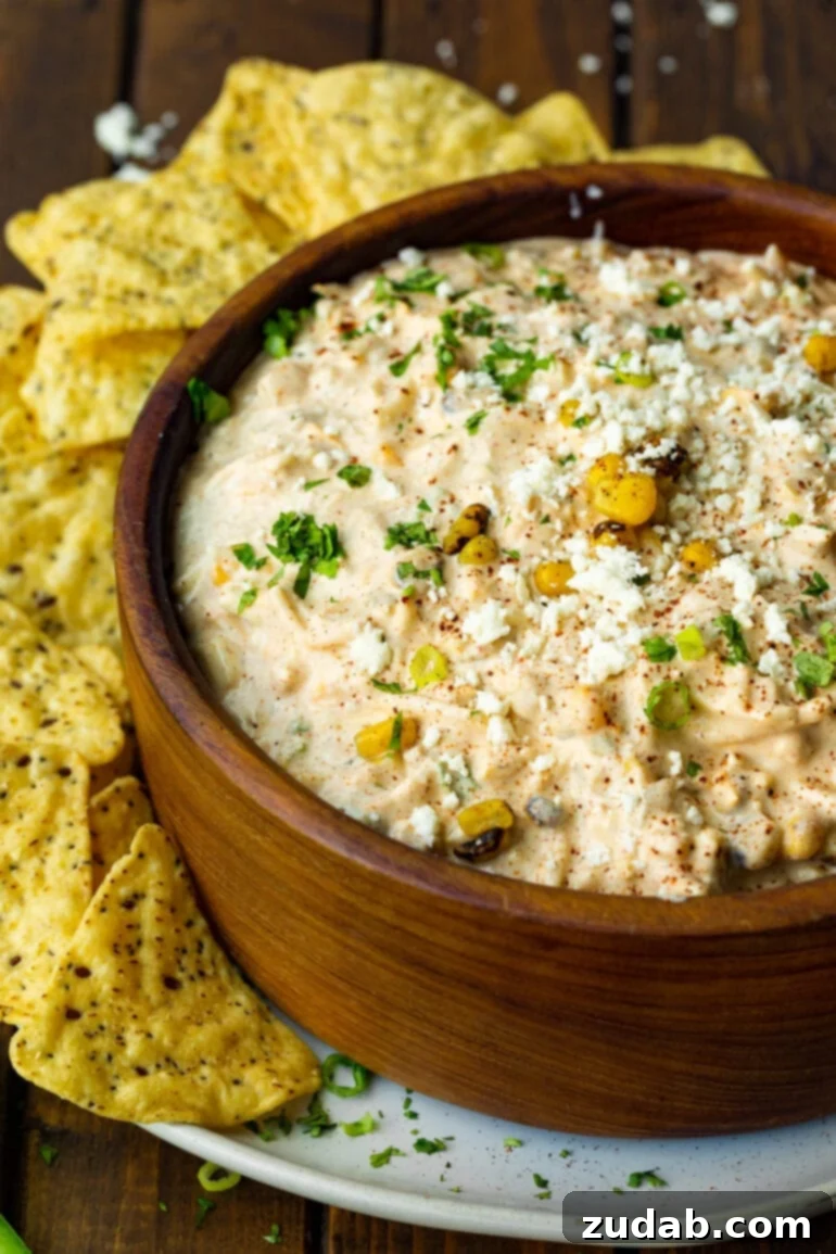 Irresistible Elote Dip 2 A large wooden bowl filled with creamy Mexican street corn dip, surrounded by a generous scattering of crispy tortilla chips, inviting guests to dig in.