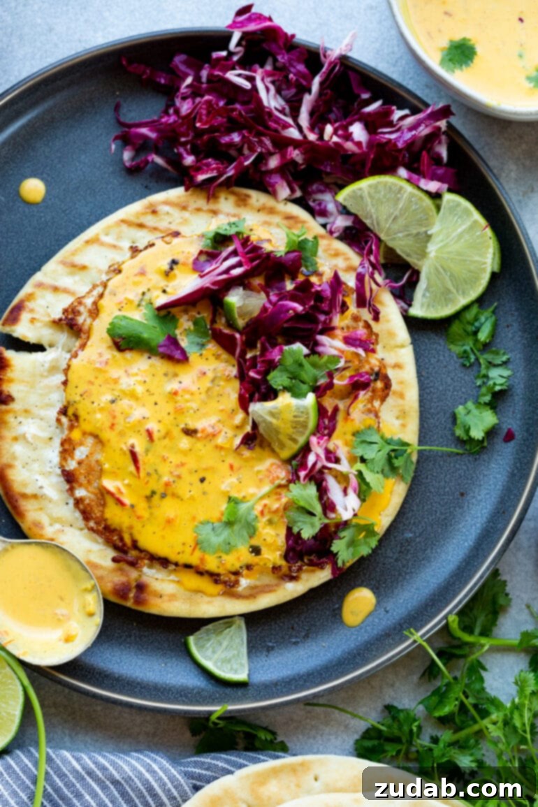 a photo of piece of pita bread topped with a thin ground chicken patty topped with coconut curry sauce and chopped radicchio and cilantro.