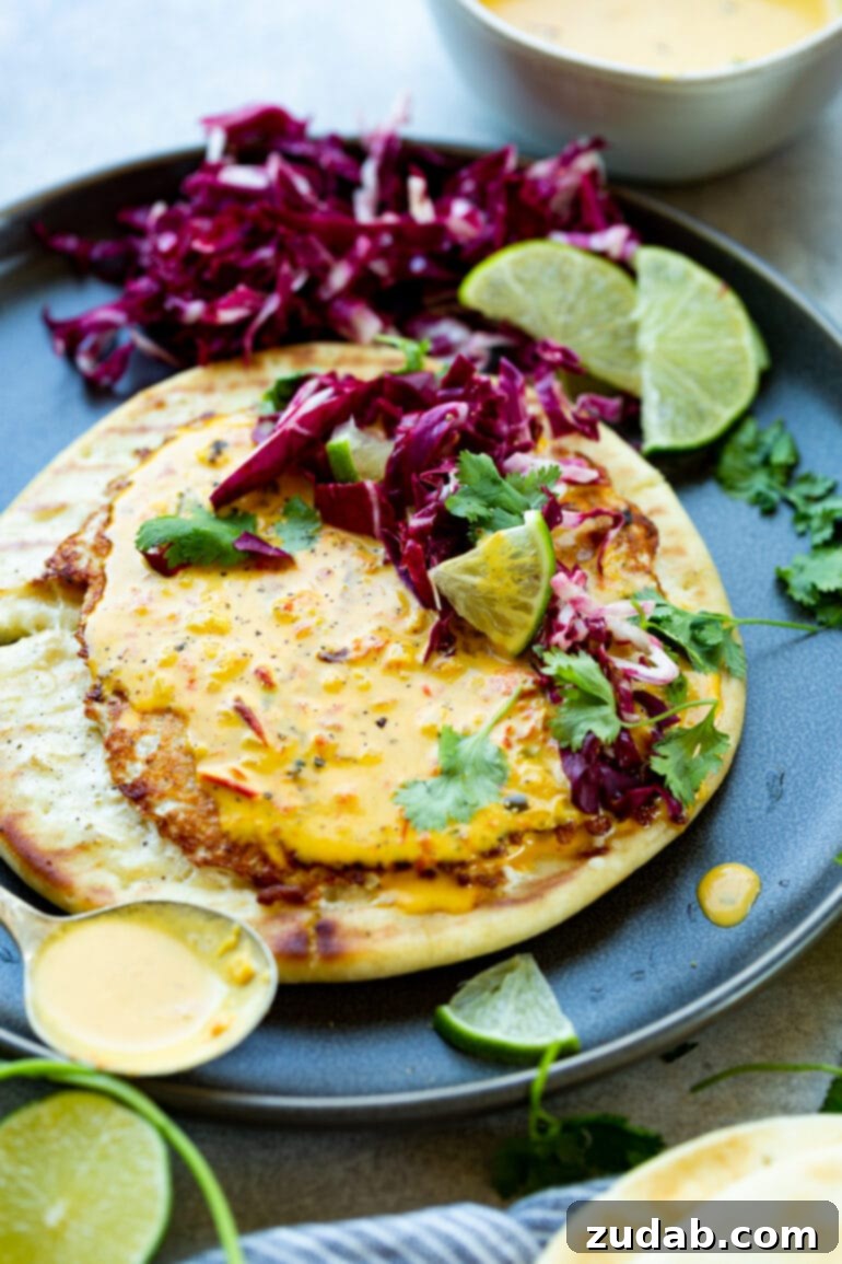 a photo of a round piece of pita bread topped with a thin cooked ground chicken patty that is topped with coconut curry sauce, chopped radicchio, cilantro and a lime wedge.
