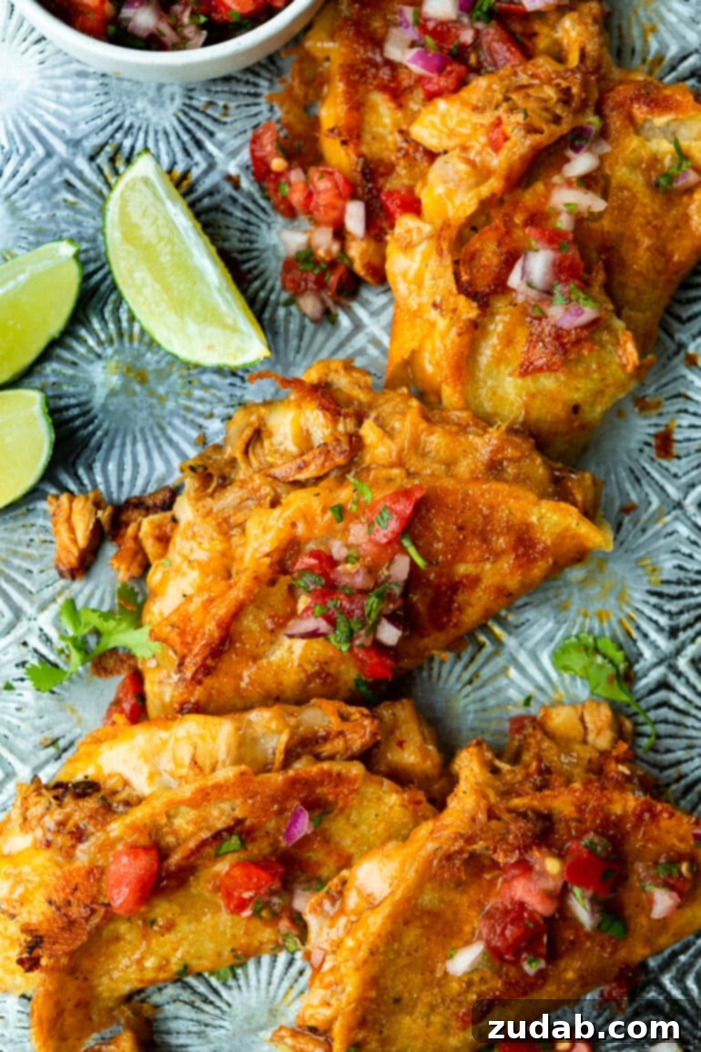 Ultimate Chicken Birria Tacos 2 A vibrant photo showcasing several golden-brown chicken birria tacos resting on a rustic metal tray, generously topped with fresh, colorful pico de gallo, inviting diners to savor their rich flavors.