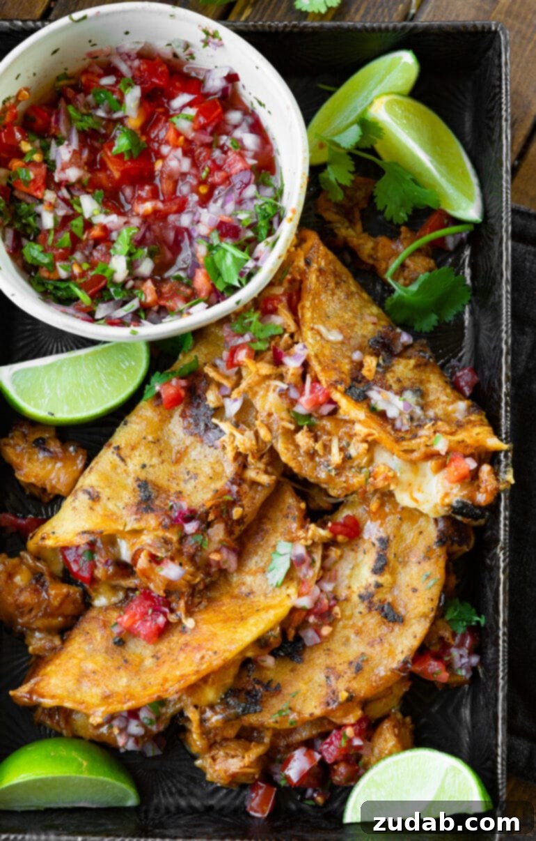 Ultimate Chicken Birria Tacos 10 A mouthwatering photo of a stack of crispy birria chicken tacos, artfully arranged on a sleek metal serving tray, with a vibrant bowl of fresh pico de gallo nestled alongside.