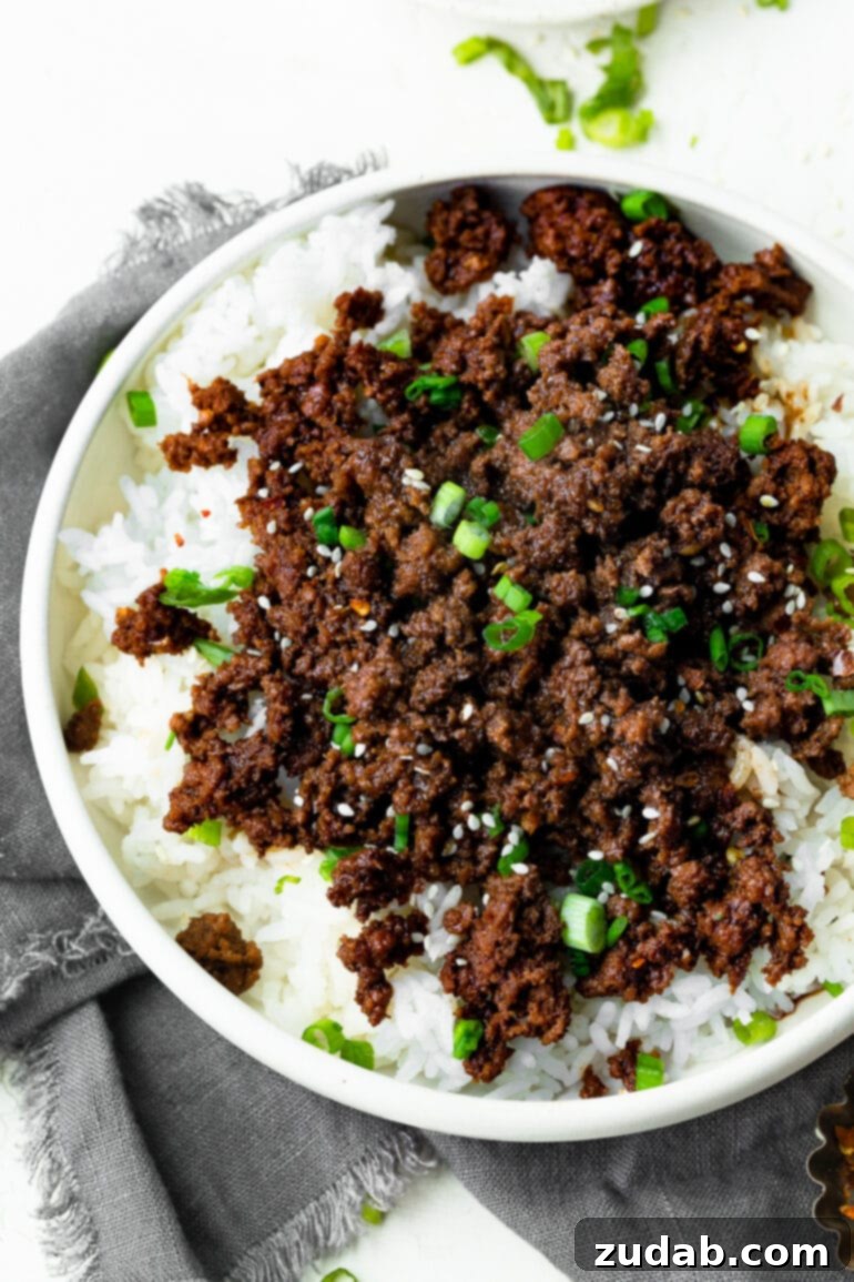 Effortless Korean Ground Beef 4 A beautifully composed shot of a bowl brimming with cooked white rice, lavishly topped with saucy Korean ground beef, vibrant sliced green onions, and a sprinkle of toasted sesame seeds.