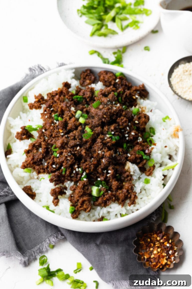 Effortless Korean Ground Beef 5 A stunning close-up of a large bowl showcasing cooked white rice, richly topped with saucy Korean ground beef, fresh sliced scallions, and a sprinkle of toasted sesame seeds.