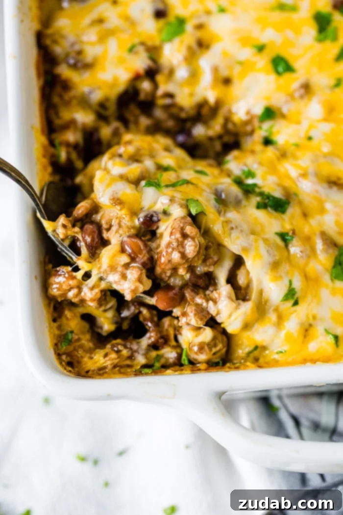 Weekly Meal Plan - September 18-24 3 A white casserole dish filled with a bubbling Mexican cheesy ground beef and rice casserole, with a large spoon scooping out a generous portion, revealing layers of savory beef, rice, beans, and melted cheese.
