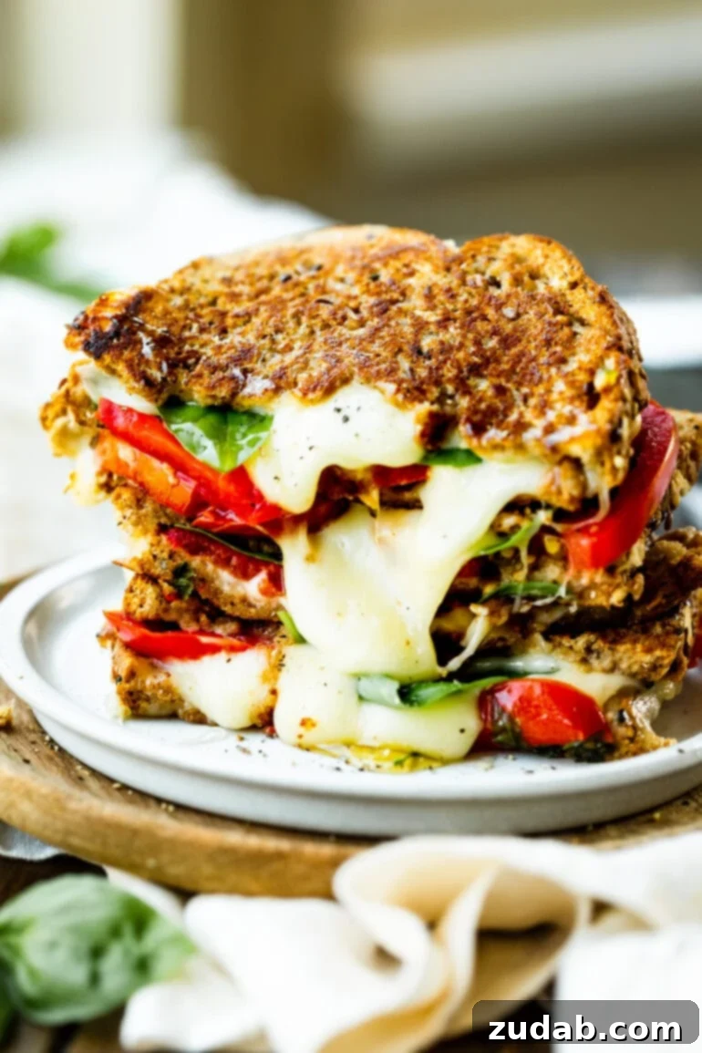 Weekly Meal Plan - September 18-24 5 A stack of several halved grilled cheese sandwiches, showcasing creamy melted Havarti cheese oozing out, layered with vibrant red tomato slices and fresh green basil leaves.