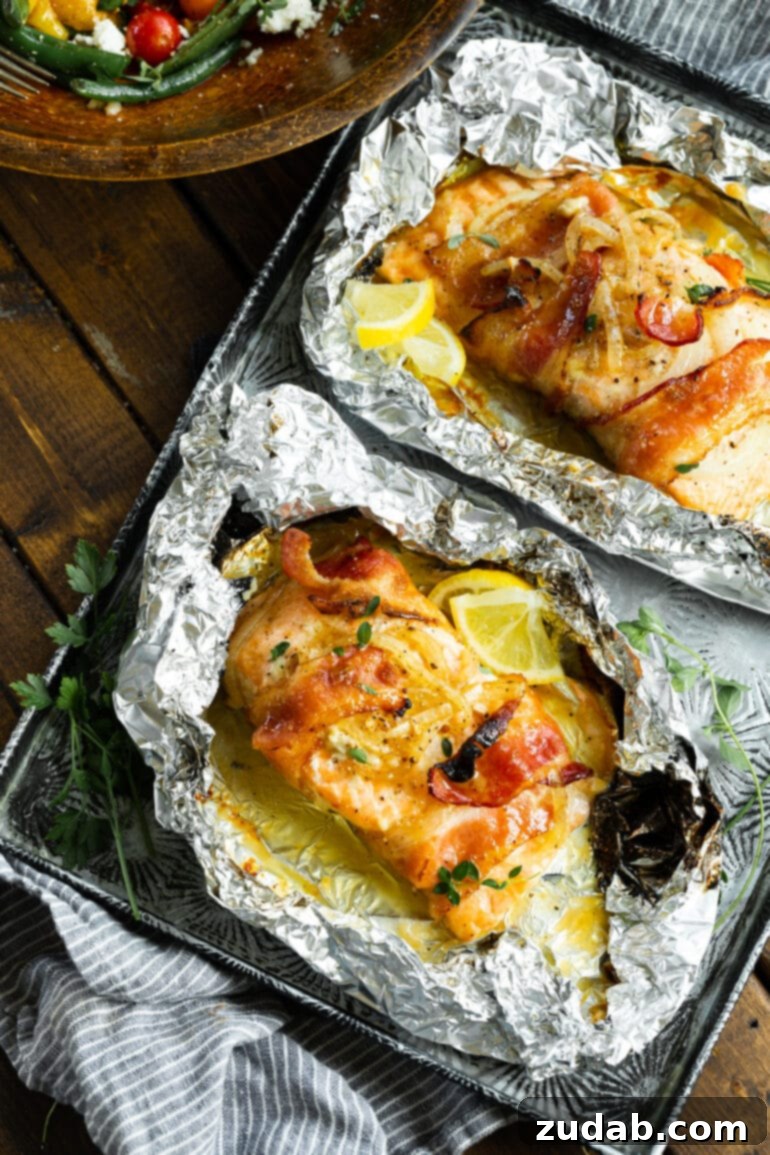 Golden Glazed Maple Bacon Mustard Salmon 3 Two baked salmon fillets, each wrapped in crispy bacon and topped with caramelized onions, resting in opened foil packets alongside fresh lemon wedges.