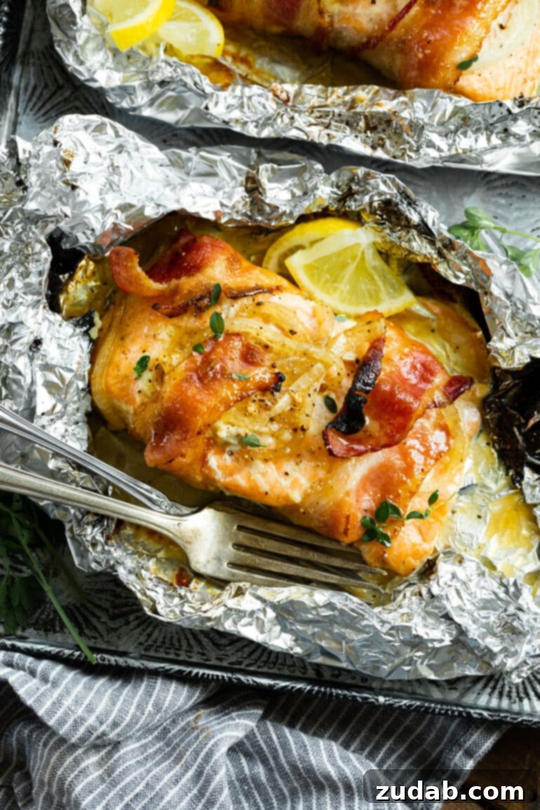 Golden Glazed Maple Bacon Mustard Salmon 5 A close-up photo of a baked salmon fillet in an opened foil packet, beautifully wrapped in crispy bacon and garnished with fresh herbs and bright lemon slices.