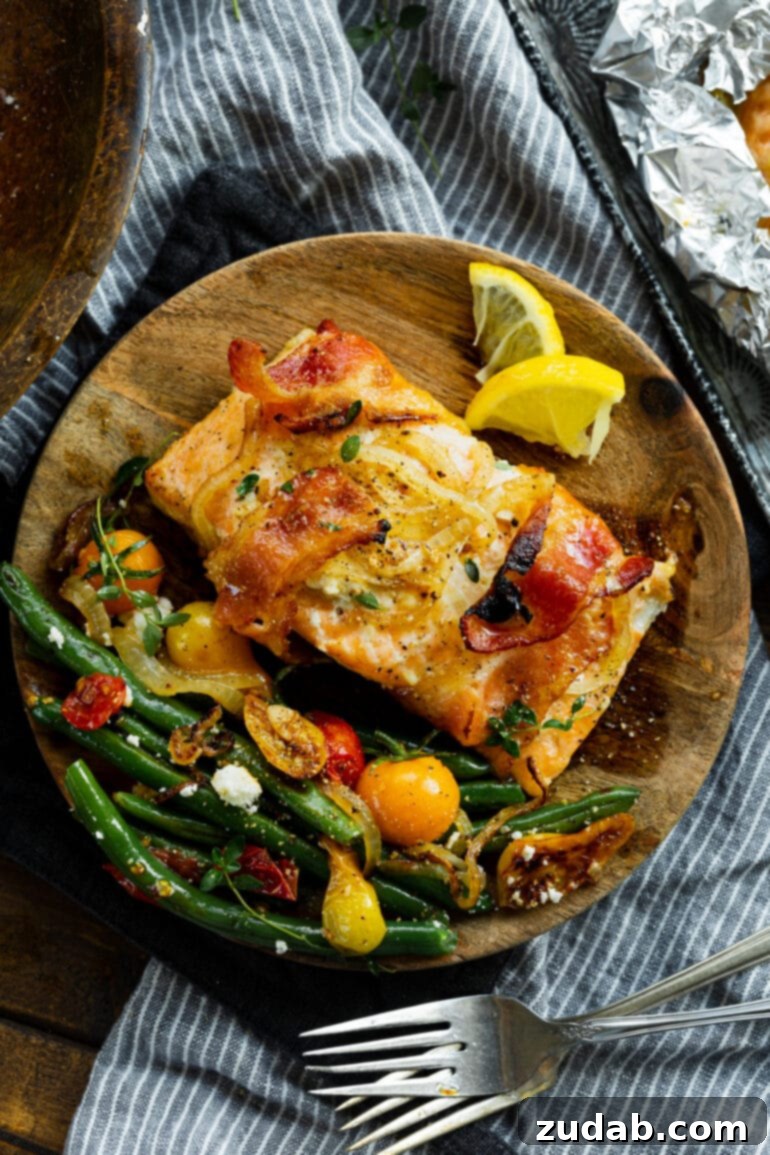 Golden Glazed Maple Bacon Mustard Salmon 6 A top-down view of a wooden plate showcasing a beautifully baked salmon fillet, wrapped in crispy bacon, served with a vibrant side of sautéed green beans and cherry tomatoes.