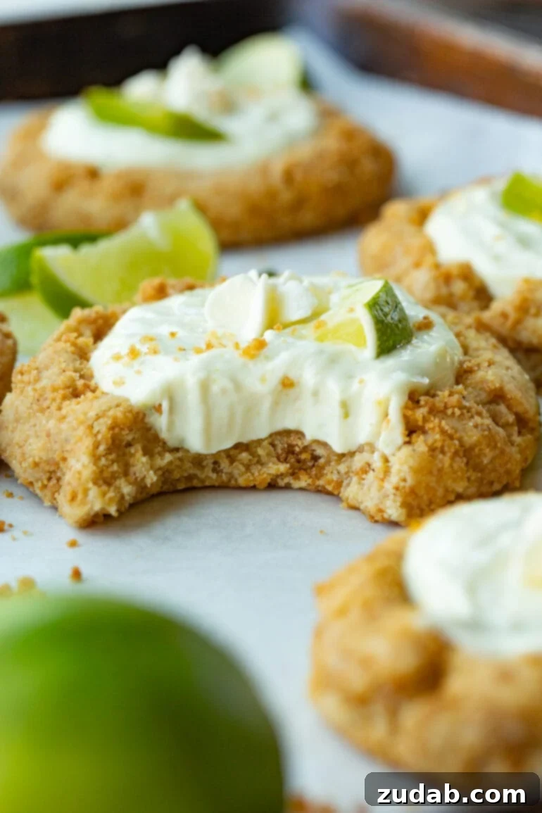Crumbl-Inspired Zesty Key Lime Pie Cookies 2 A photo of a key lime pie cookie that has had a bite taken out of it so you can see the creamy filling inside the graham cracker crust cookie topped with a small slice of fresh lime.