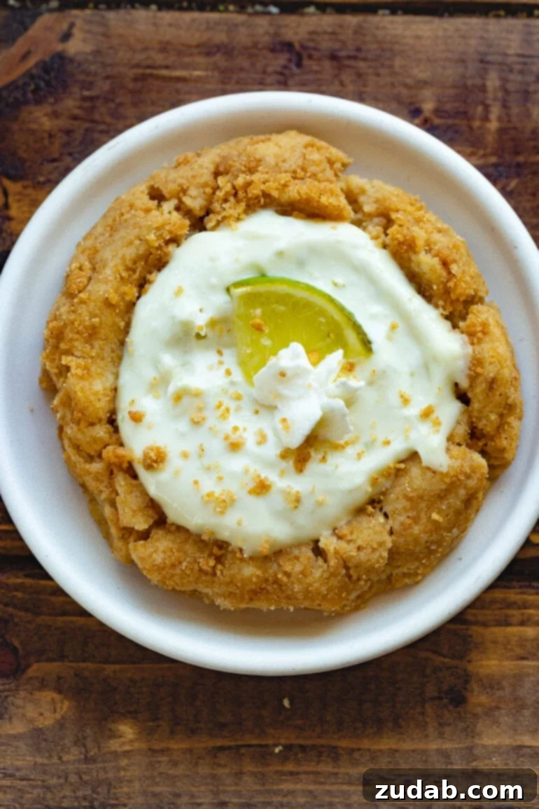 Crumbl-Inspired Zesty Key Lime Pie Cookies 3 A photo taken over the top of a key lime pie cookie topped with a wedge of fresh lime and a small dollop of whipped cream.