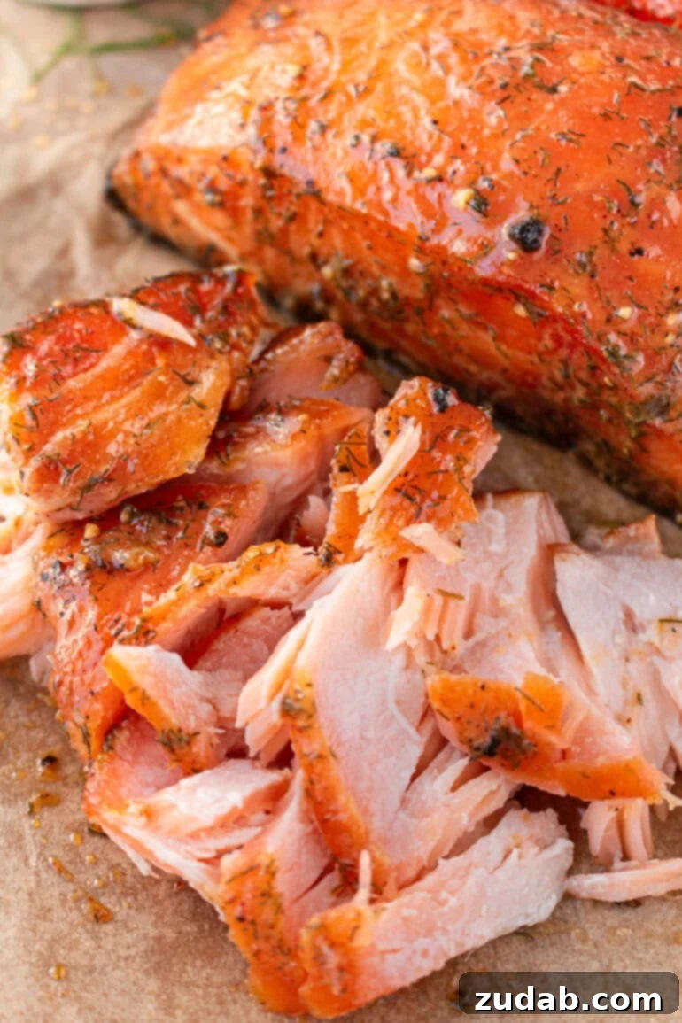 Perfect Smoked Salmon Recipe 3 a close-up photo of a beautifully flaked smoked salmon fillet, showcasing its moist and tender texture, next to a whole smoked fillet
