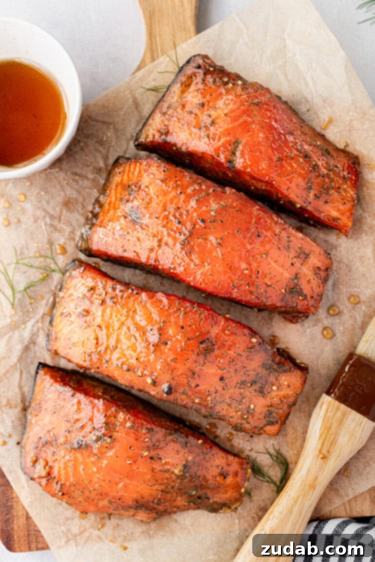 Perfect Smoked Salmon Recipe 4 a photo of 4 smoked salmon fillets sitting on parchment paper, beautifully glazed, next to a small cup of maple syrup glaze