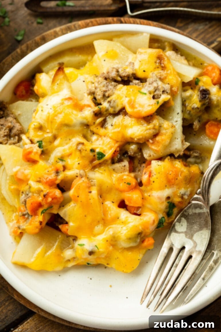 Hearty Cheesy Beef and Potato Bake 2 A vibrant photo of a dinner plate featuring a generous serving of cheesy ground beef and potato casserole, accompanied by two forks, ready to be enjoyed.