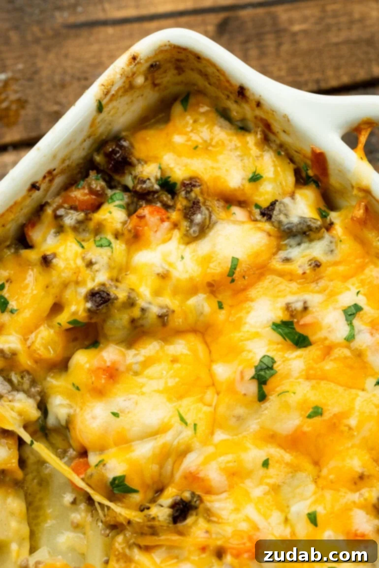 Hearty Cheesy Beef and Potato Bake 5 A white square baking dish, brimming with cheesy ground beef and potato casserole, is shown from a high angle, topped with a perfectly melted, golden-brown cheese crust.